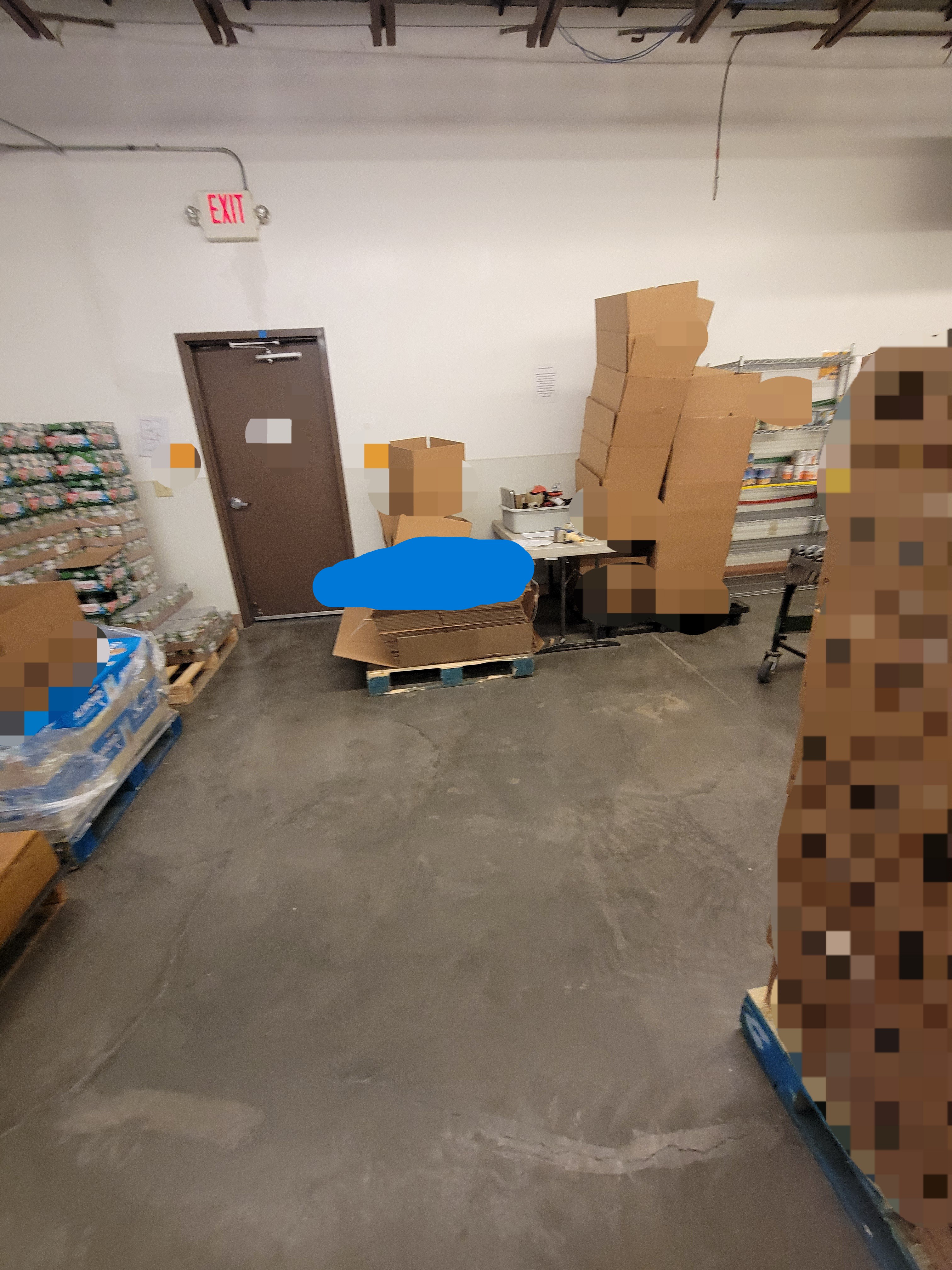 Warehouse area with a door in front with boxes, pallets of food, shelves, and table around it.